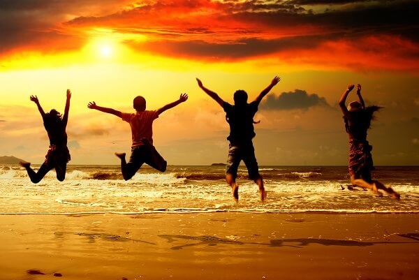 Travelling friends jumping at the beach with sun setting in background