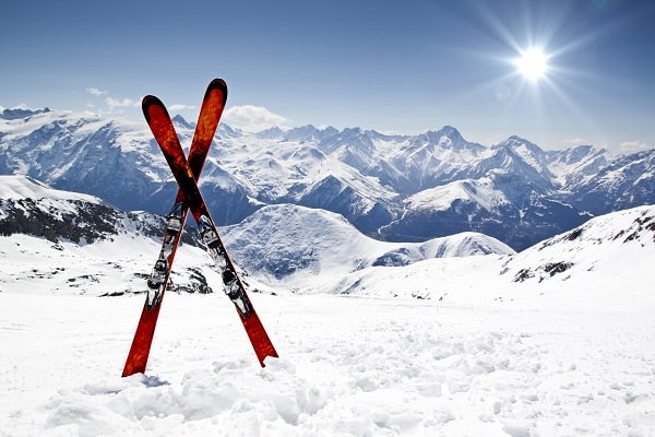 Two red and black skis standing in the snow with mountains in background