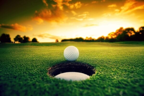 Golf ball balancing on edge of hole with stunning sunset in background