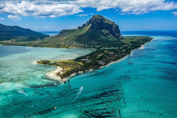 green mountain extending into the turquoise ocean with a cloudy blue sky